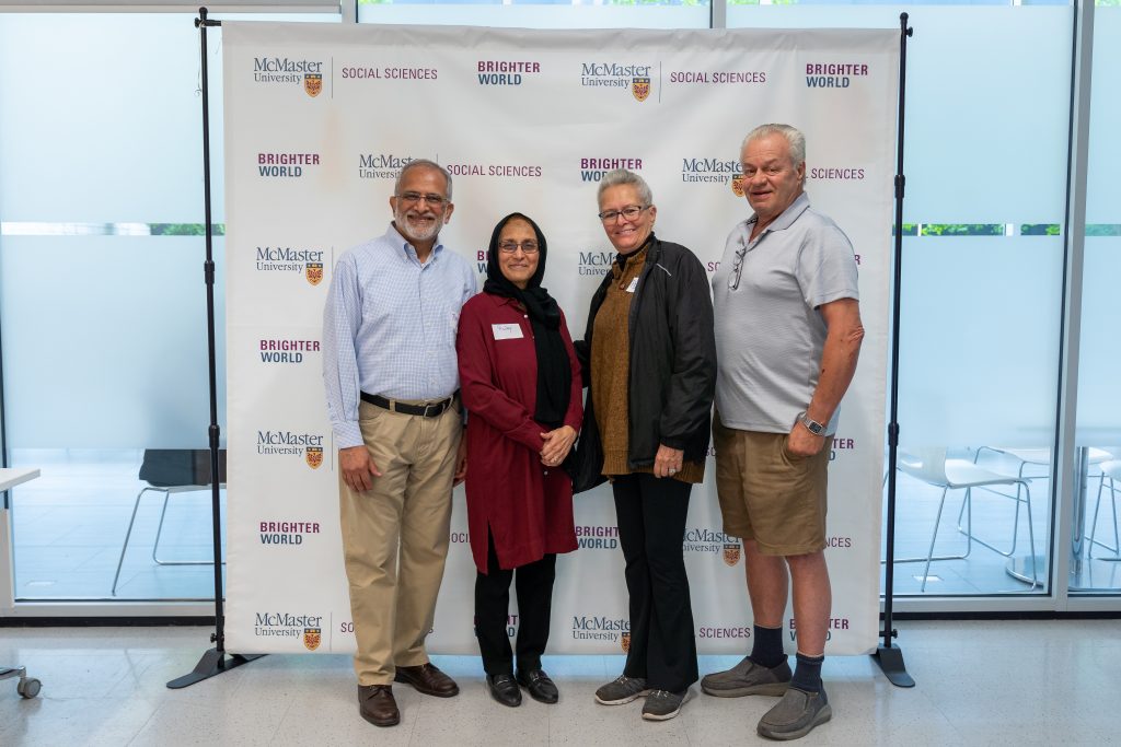 Image features 4 SHARE Group volunteers standing together, posing in front of the McMaster Faculty of Social Sciences backdrop.